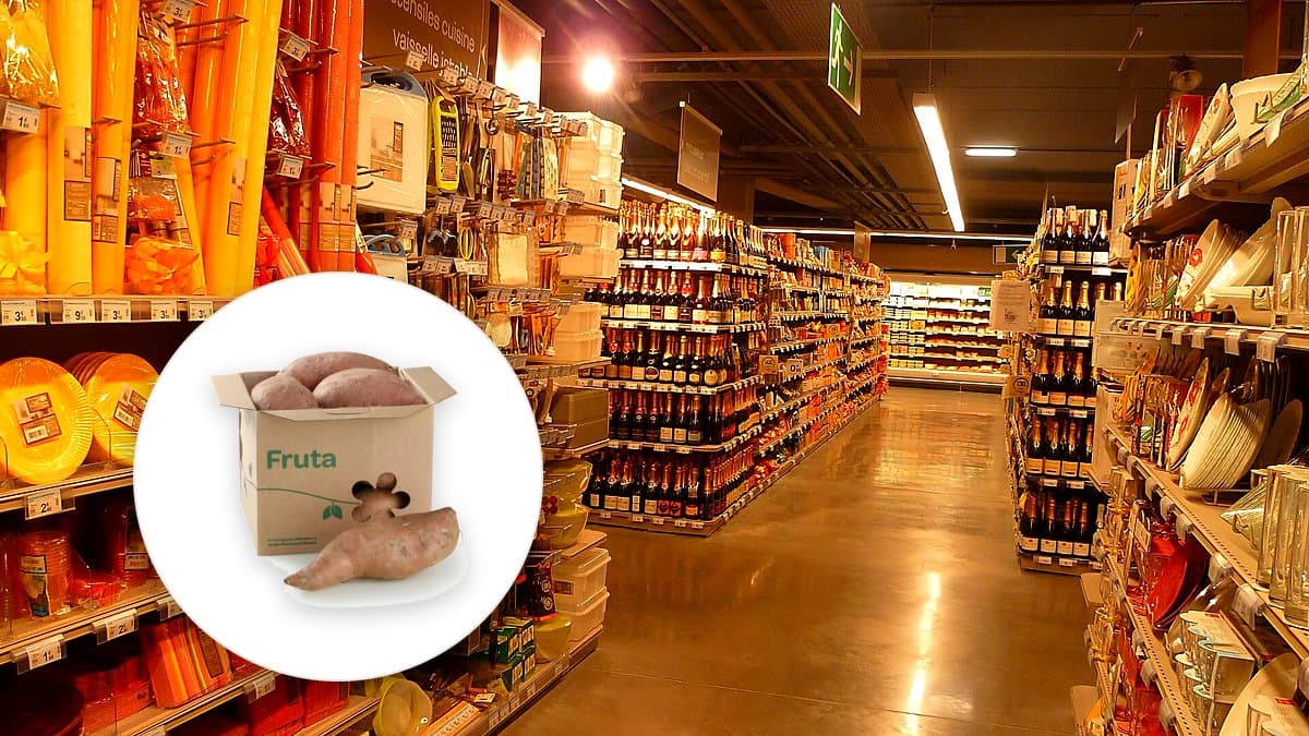 Boniatos naranja frescos en bandeja de caja de madera en frutería de supermercado español, uno cortado mostrando su pulpa vivida, luz de mañana suave